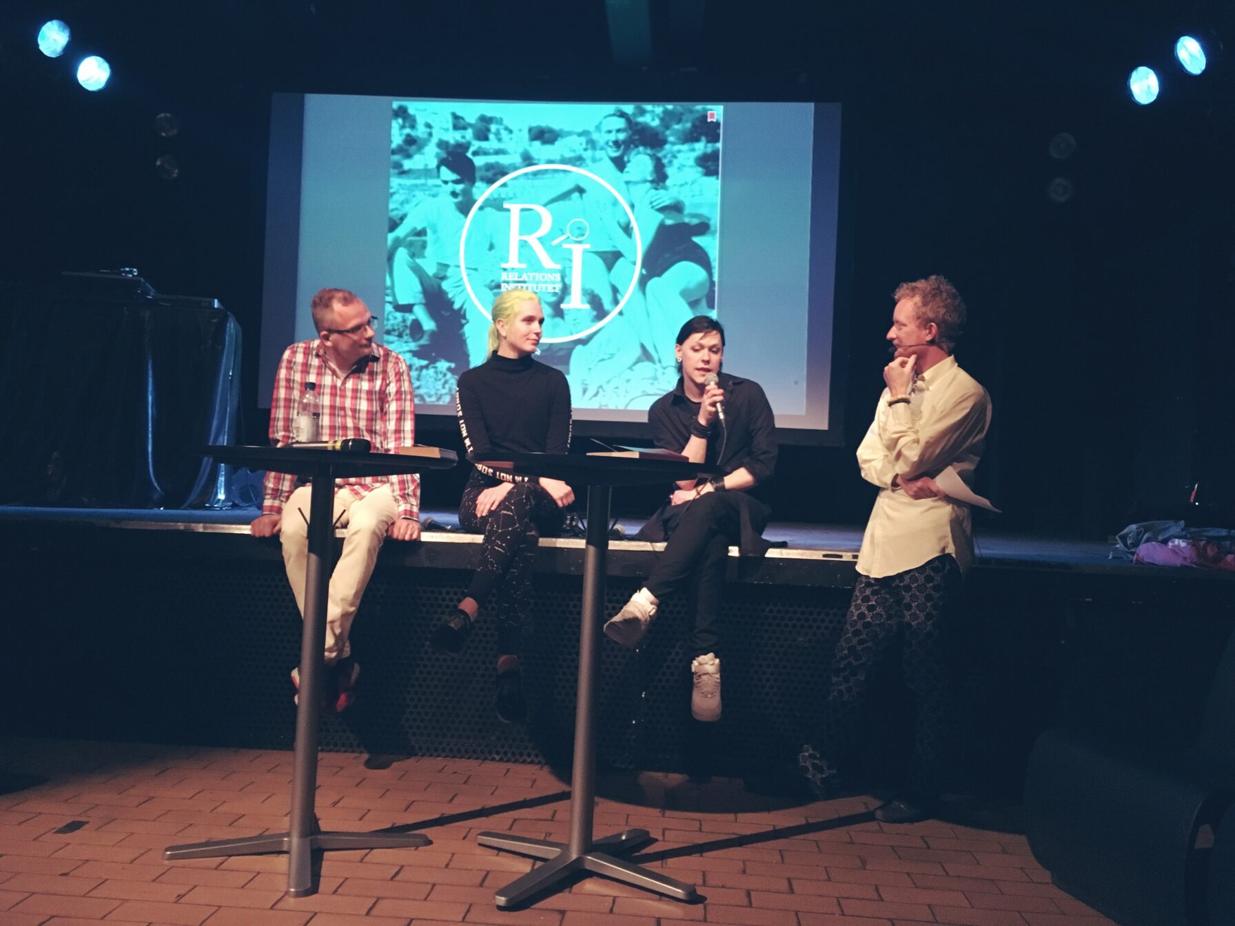 Fyra paneldeltagare på scenkanten i en mysig klubblokal